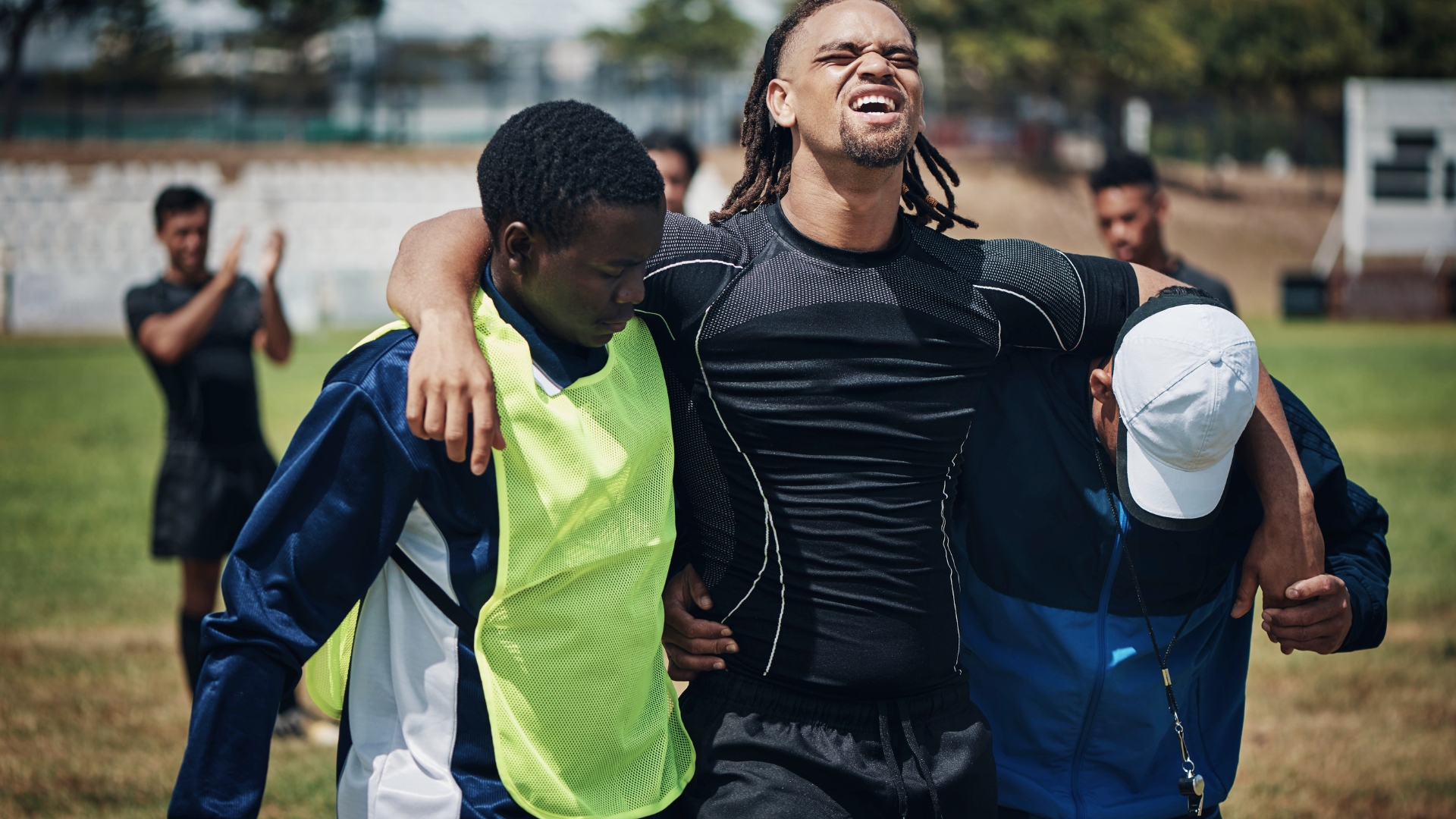 Injured footballer being supported off the pitch by teammates
