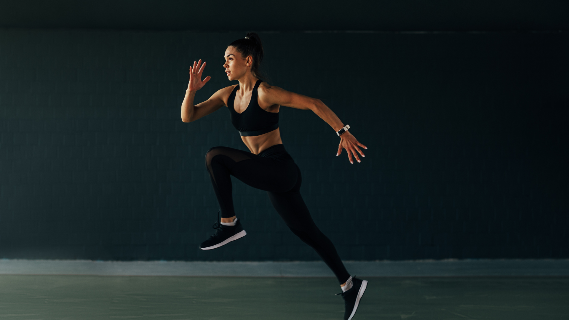 Female sprinter mid-stride against a dark wall, focused intensity